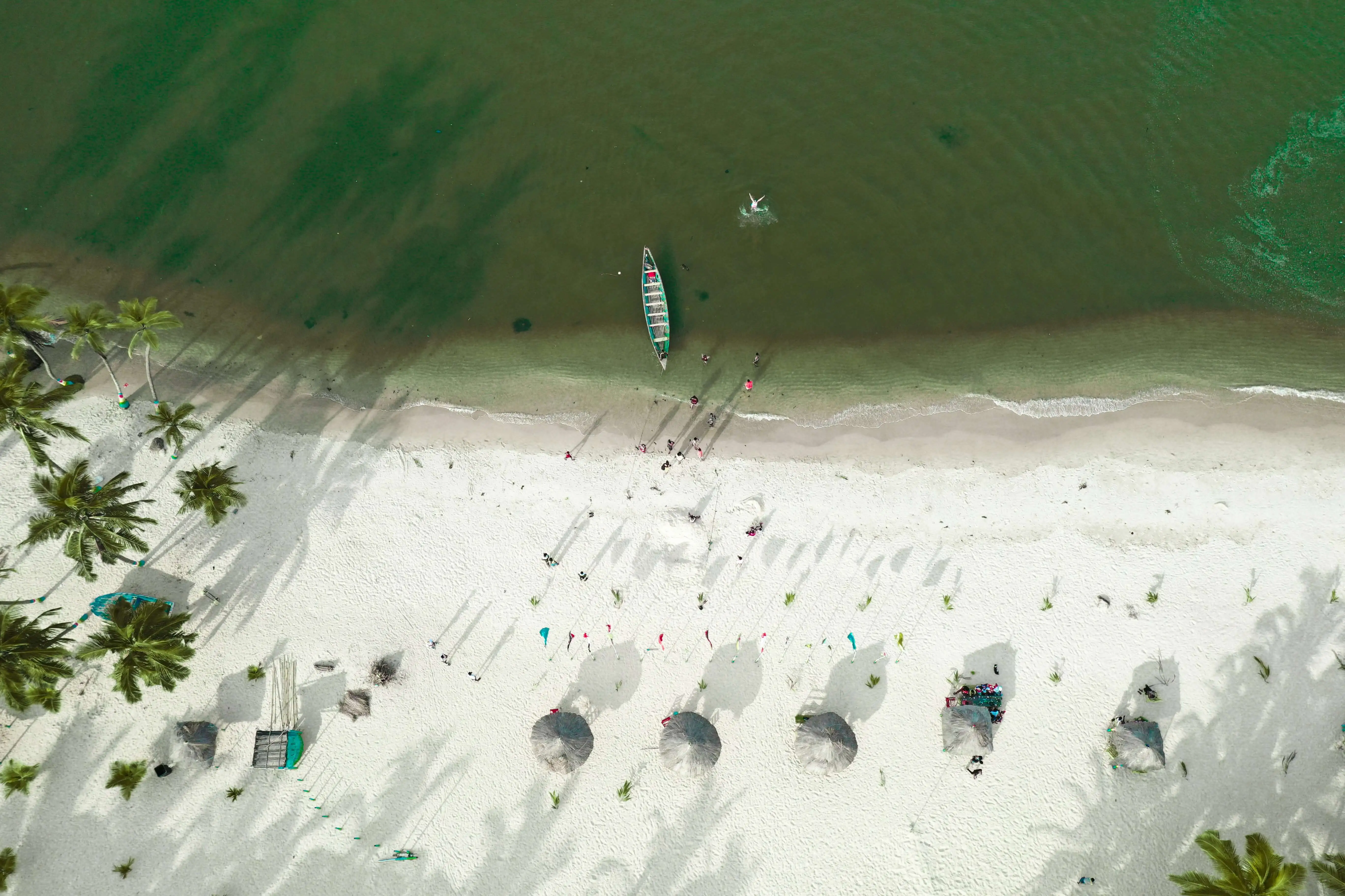 Aerial view of beach with colorful umbrellas and boats in the water.